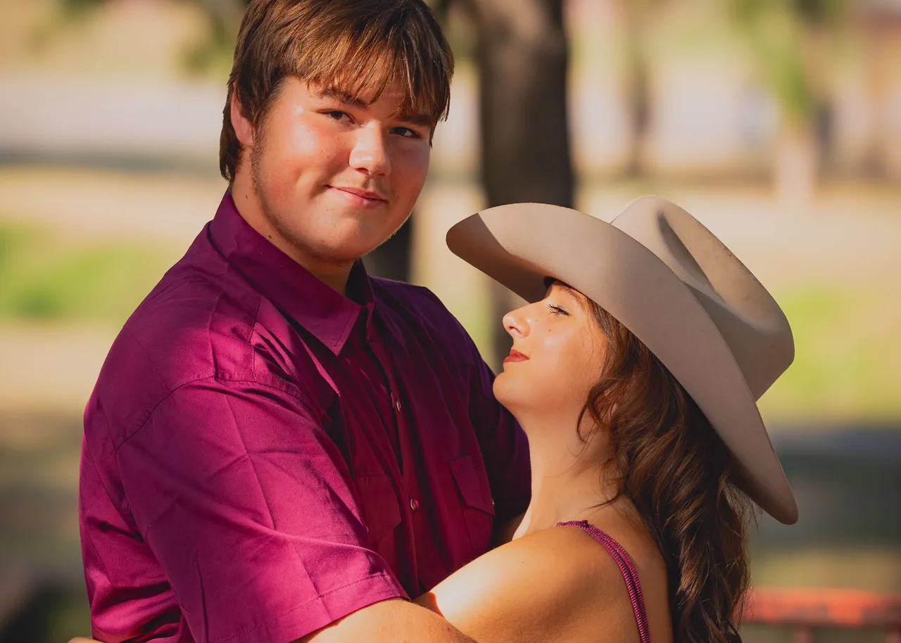 She wears his cowboy hat while he smiles at the camera