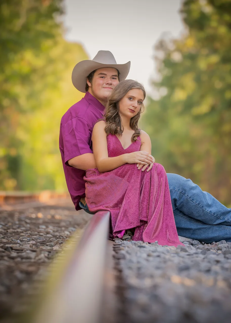 A couple seated on a rail with trees fading into the distance