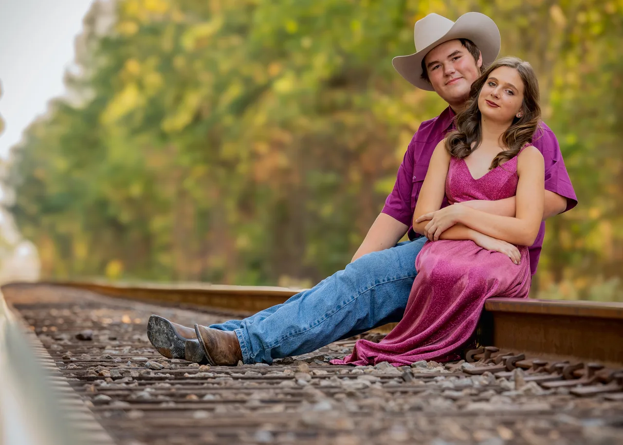 A couple sitting close together on railroad tracks at golden hour