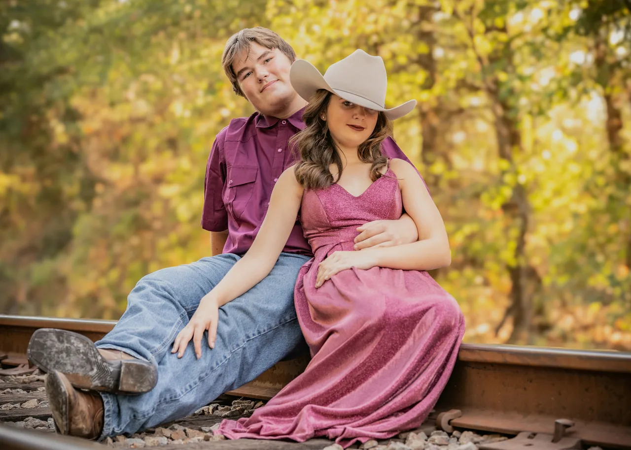 A couple sitting on railroad tracks under golden fall trees