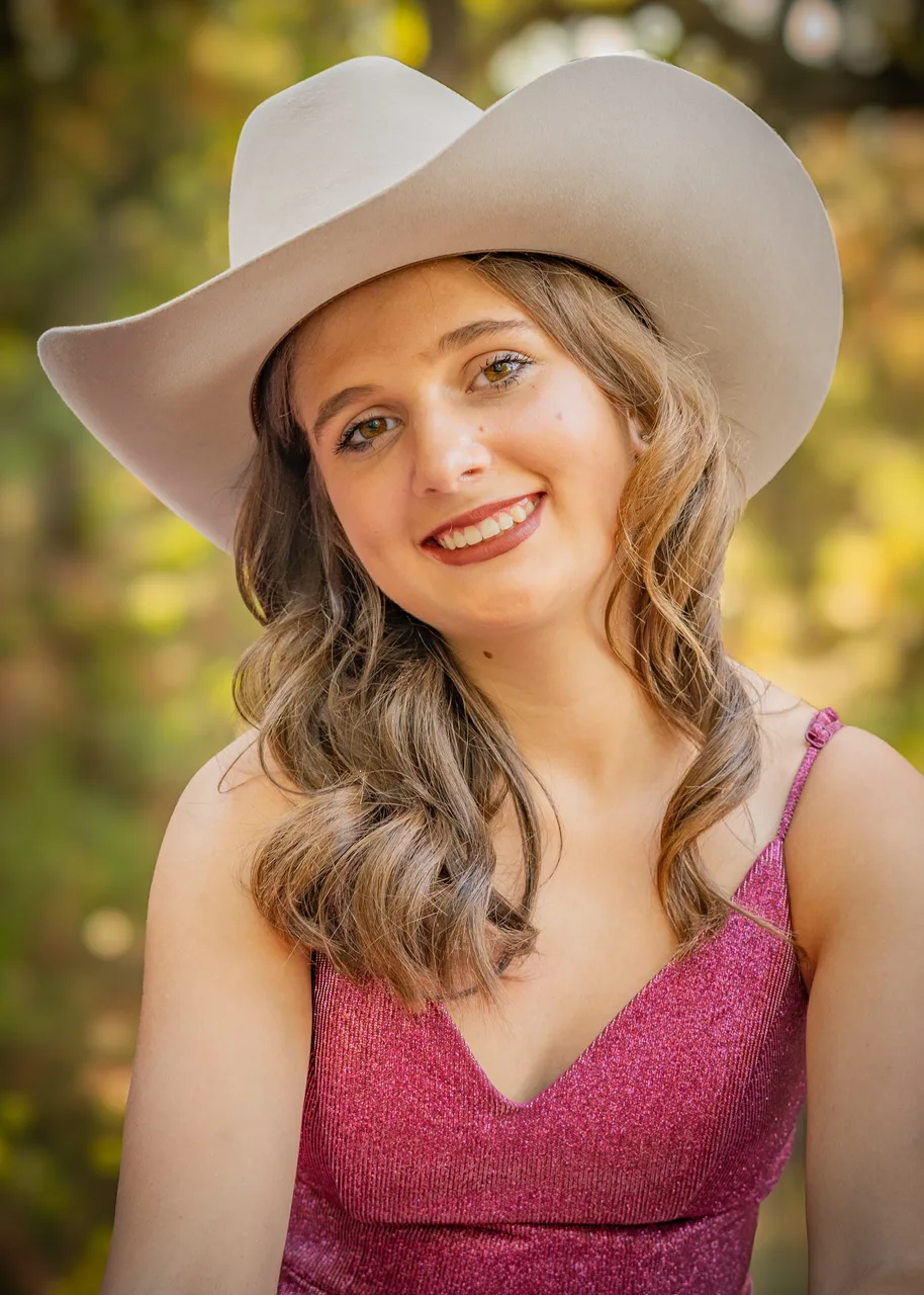 A smiling portrait in a cowboy hat with fall color behind