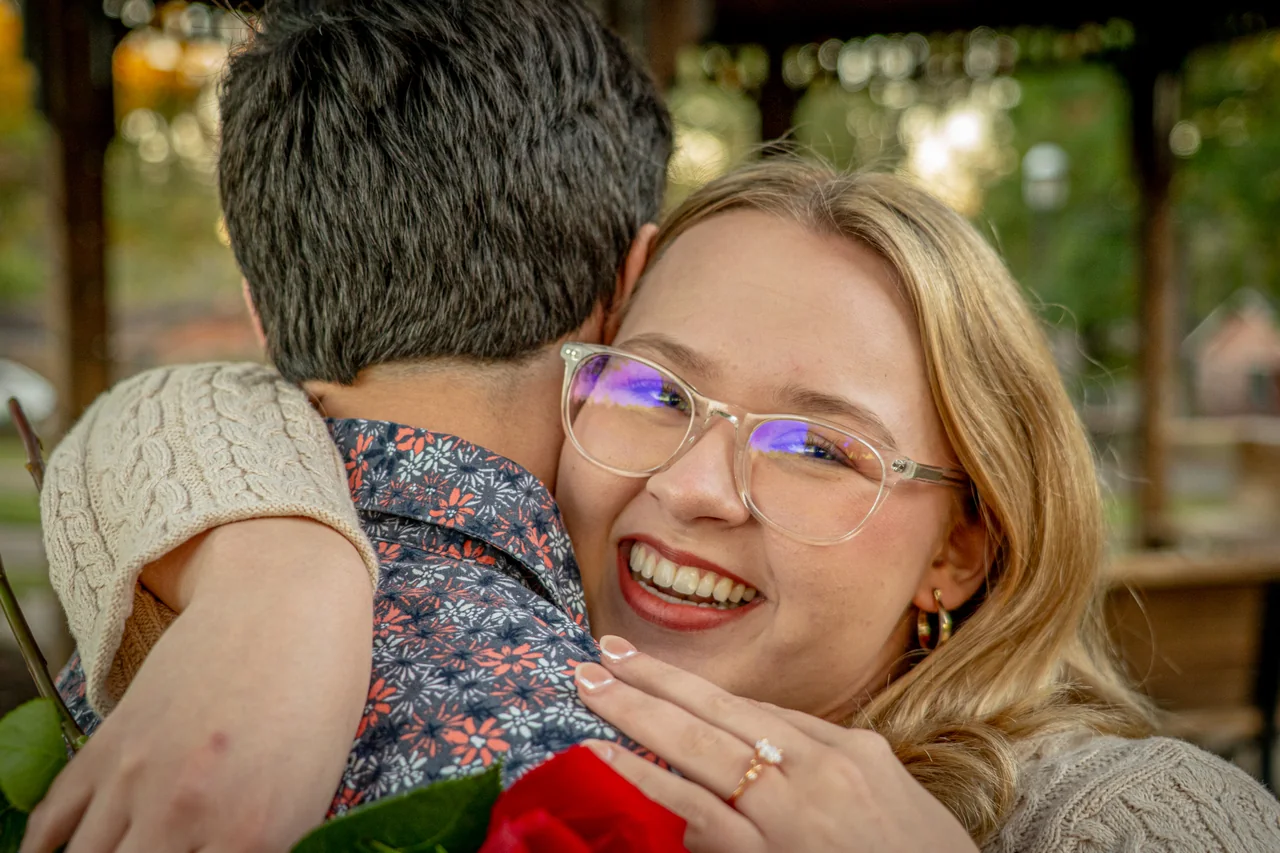 She hugs him and shows her new engagement ring, laughing