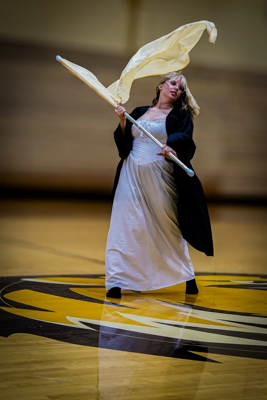 A color guard senior spinning a flag in the gym