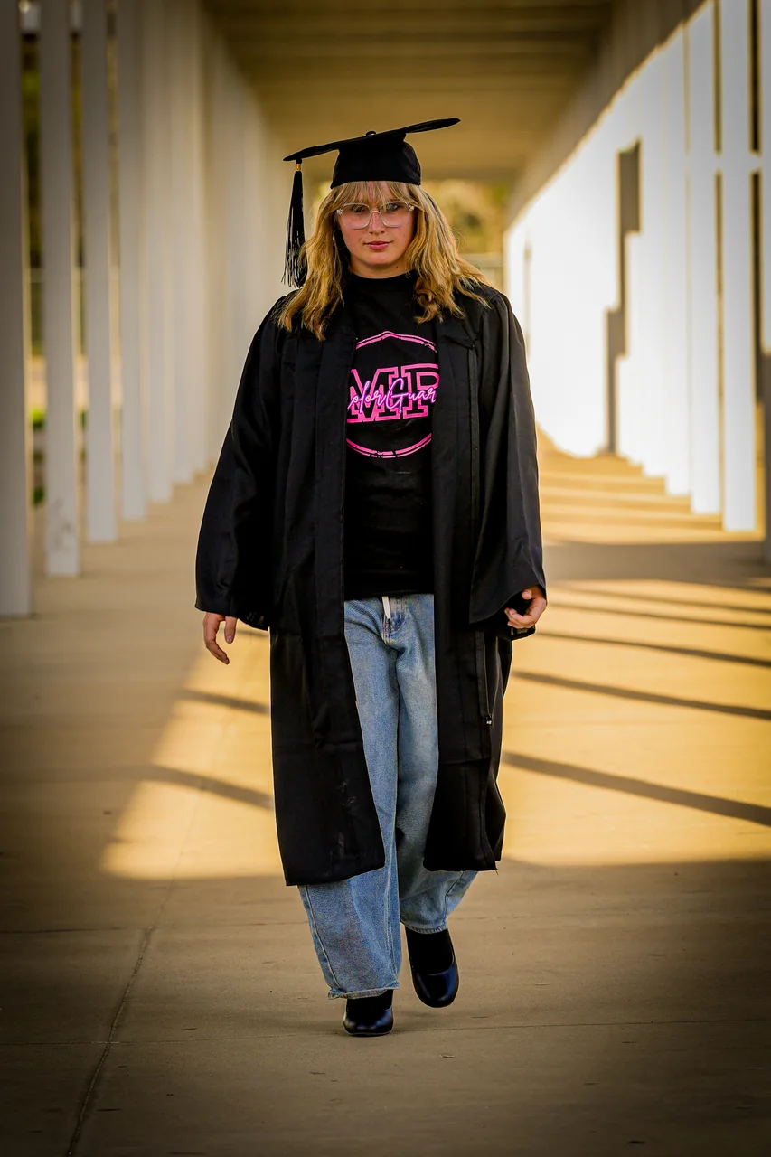 A graduate walking down a sunlit colonnade in her gown